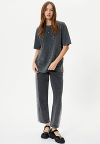 Camiseta gris de gran tamaño con acentos de tachuelas, combinada con jeans de pierna ancha gris oscuro y zapatos de plataforma negros de charol.