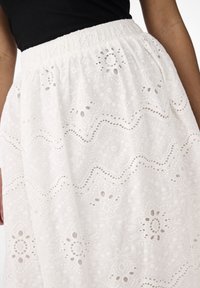 Hvit brodert skjørt med elastisk strikk i livet, prydet med intrikate blomsterdesign og bølgende kanter. Lett stoffsammensetning.