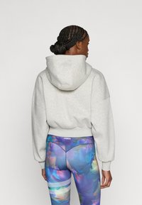 Ανοιχτό γκρι κοντό φούτερ με κουκούλα και κορδόνι, καθώς και με ριμπ λαιμόκοψη, συνδυασμένο με πολύχρωμο κολάν που διαθέτει λουλουδάτα μοτίβα και πλαϊνές ρίγες.