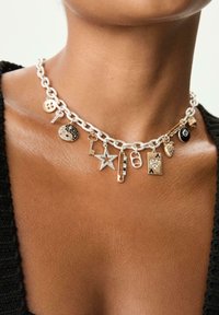 Collana in argento con vari ciondoli, tra cui uno yin-yang, una stella, una chiave, una carta da gioco e un pulsante, caratterizzata da materiali e texture miste.