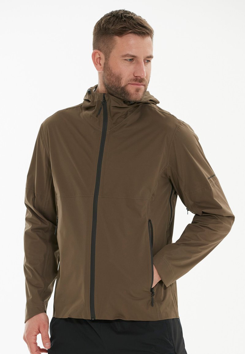 Veste légère marron avec capuche, fermeture éclair à l'avant, poches latérales et poignets zippés. Texture lisse et design minimaliste.