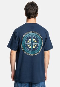 Navy blue cotton t-shirt featuring a large compass graphic on the back, with text and star details in yellow and turquoise accents.