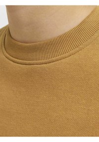 Suéter de algodón marrón con un cuello de canalé y una superficie suave y texturizada. La vista en primer plano resalta los detalles del color y la costura.