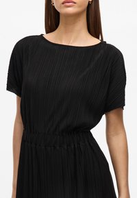 Vestido preta plissado com mangas curtas, gola redonda, cintura elástica e uma silhueta fluida, feito de tecido leve.