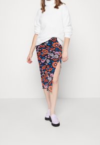 Gonna midi floreale con uno spacco alto, caratterizzata da uno sfondo nero e fiori colorati arancioni, viola e blu; abbinata a un maglione bianco e scarpe lilla.