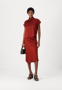 Top in raso rosso con maniche corte, abbinato a una gonna midi in raso rosso aderente. Borsa nera e sandali con tacco a blocco aperti.