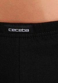 Ceinture en coton noir avec couture visible ; présente une étiquette de logo blanche portant l'inscription "ceceba". Texture lisse, matériau élastique.