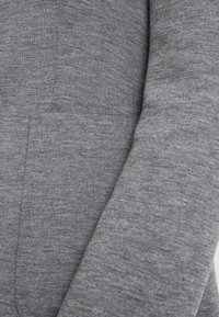 Tessuto grigio con trama testurizzata e aspetto liscio, caratterizzato da una cucitura piatta su un capo di abbigliamento, evidenziando morbidezza ed elasticità.