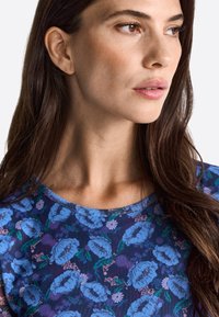 Top con un estampado floral de flores azules sobre un fondo azul oscuro, con escote redondo y mangas cortas. Textura de tela suave.
