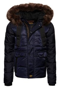 Giacca puffer blu navy con cappuccio rifinito in pelliccia sintetica, spallacci neri, due tasche a patta e una tasca laterale con zip. Finitura testurizzata.