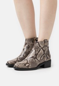 Bottines en peau de serpent marron et beige, avec fermeture éclair latérale, talon carré et finition texturée avec un motif géométrique subtil.