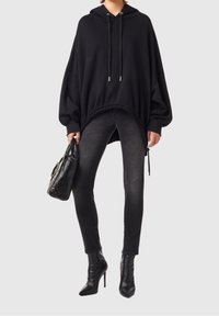 Översize svart hoodie med dragsko i huvan och ribbad nederkant, kombinerad med tajta svarta jeans och spetsiga svarta klackstövlar.