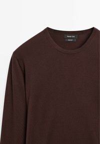 Maglietta a maniche lunghe con collo a giro in cotone bordeaux scuro. Presenta una texture liscia e un'etichetta che indica 100% cotone. Design semplice e classico.