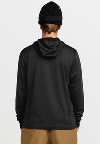 Un sweat à capuche noir en tissu texturé, doté d'une capuche, de manches longues et d'une coupe décontractée. Porté avec un bonnet en tricot noir.