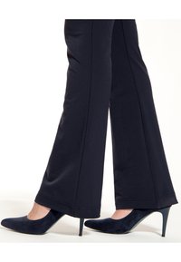 Marineblauwe wijde broek van zachte stof, gedragen met gladde, puntige marineblauwe pumps met een stilettohak. Subtiele naaddetails zichtbaar.