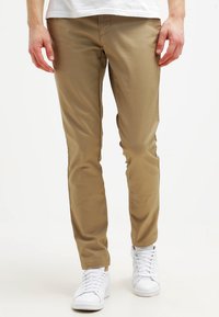 Beige chino's van zachte stof, met een slim fit ontwerp, platte voorkant en klassieke vijf-pocket stijl, gecombineerd met witte sneakers.