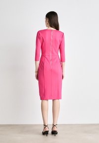 Fitted pink dress with three-quarter sleeves and a rear zipper. Smooth fabric texture and knee-length design with subtle side seams.