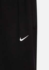 Pantalons de survêtement noirs en tissu doux, avec un logo Nike blanc sur le côté gauche. Comprend des poches et une taille élastique.