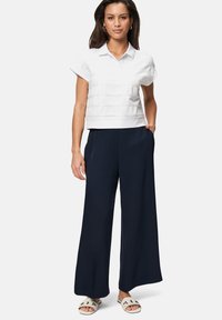 Haut à col blanc à manches courtes avec des lignes de texture horizontales, associé à un pantalon large navy et des sandales de couleur claire.