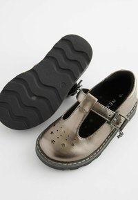 Metallisch bronze Farbe Schuhe mit einem Ausschnitt-Design, das Sternmuster zeigt, mit einer Schnalle gesichert. Texturierte schwarze Gummisohle mit einem wellenförmigen Profil.