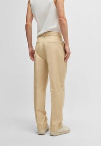 Beige trousers with a straight-leg design, made of smooth fabric. Features two rear pockets with subtle stitching details.