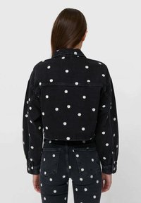 Czarna dżinsowa kurtka z białą haftowaną stokrotką, krótka konstrukcja i długie rękawy. Tekstura jest solidna z zapinanymi mankietami.