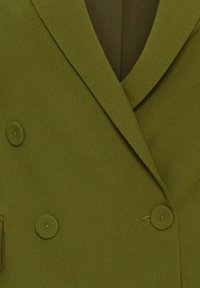 Blazer vert olive à double boutonnage avec larges revers et boutons recouverts du même tissu.