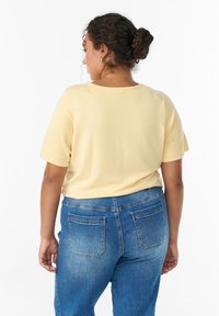 Gelbes Kurzarmshirt mit rundem Ausschnitt und glatter Textur. Kombiniert mit blauen Jeans aus Denim, die klassische Gesäßtaschen und ein verwaschenes Design aufweisen.