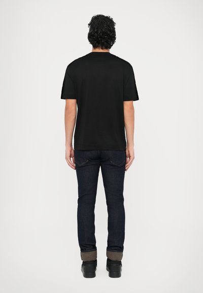 Juoda medvilninė marškinėliai laisvo silueto, derinami su tamsiai mėlynomis džinsinėmis kelnėmis. Turi lygų tekstūrą ir trumpas rankoves.