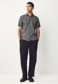 Camicia nera a maniche corte con bottoni e motivo geometrico, abbinata a pantaloni scuri e scarpe nere, per un look coordinato.