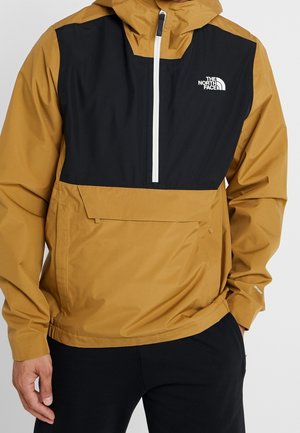 Braune und schwarze North Face Jacke mit halb geöffnetem Reißverschluss vorne, Kapuze und großer Fronttasche, getragen von einer Person mit den Händen in den Taschen.