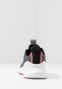 Zapato deportivo gris y negro con acentos en color coral, suela blanca y tira de agarre, mostrado desde la parte trasera sobre una superficie y fondo blancos.