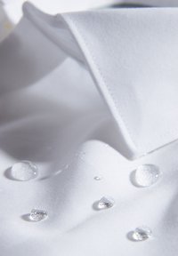 Witte stof met zichtbare waterdruppels op een glad oppervlak; beschikt over een kraagrand en textuur die wijzen op een formeel overhemdontwerp.
