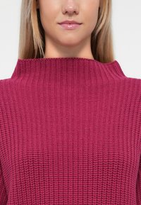 Pulôver de malha canelada em rosa escuro com um decote alto. Apresenta um padrão texturizado, evidenciando pontos uniformes e um ajuste descontraído.