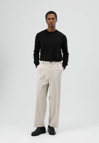 Zwart shirt met lange mouwen, beige wijde pantalon met plooien aan de voorkant, zwarte schoenen; gladde stof met een getailleerde pasvorm, geen zichtbare patronen.