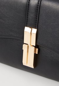 Borsa a mano in pelle nera con superficie texture, chiusura in metallo dorato e un design elegante e strutturato. Minimalista e con linee pulite.