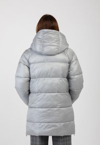 Cappotto puffer grigio con cappuccio, caratterizzato da un design trapuntato e una texture lucida e liscia. Tasche con zip ai lati.
