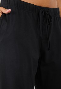 Pantalons jogger en coton noir avec une taille élastique et un cordon de serrage. Comprend des poches latérales et une texture douce et lisse.