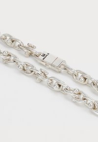 Collar de cadena de plata con acentos de bolitas redondas y un cierre rectangular grabado con la palabra "MAPLE" sobre un fondo blanco.