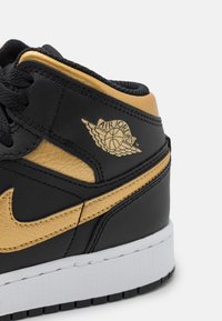 Črne in zlate usnjene superge z teksturirano površino, oblazinjenim ovratnikom in belim podplatom, z vidnim logotipom Air Jordan na strani.
