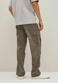 Pantaloni cargo in verde oliva, con più tasche laterali, una vestibilità ampia e tessuto resistente. Abbinati a sneaker bianche.