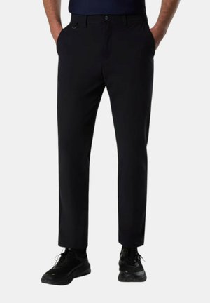 Uomo che indossa pantaloni neri a gamba dritta con tasche laterali e sneakers nere, in piedi con le mani nelle tasche su sfondo bianco.