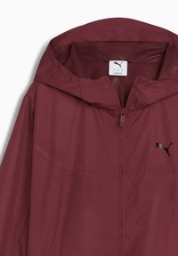 Rote leichte Jacke mit einem meshgefütterten Kapuze, ausgestattet mit einem Frontreißverschluss und einem dezenten schwarzen Puma-Logo auf der Brust. Glatte Textur.