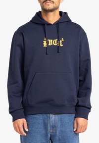 Navy blue cotton hoodie with a front pouch pocket, drawstring hood, and yellow logo text. Soft texture, casual fit, ribbed cuffs and hem.