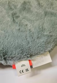 Tela de felpa de color gris claro con una textura suave y peluda. Incluye una etiqueta con un logotipo y certificaciones de seguridad. Acentuada con una sección roja.