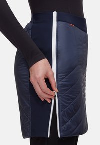 Quiltad marinblå kjol med vit dragkedjedetalj. Har en hög midja och diagonalt quiltat mönster. Materialet har en slät, något glänsande yta.