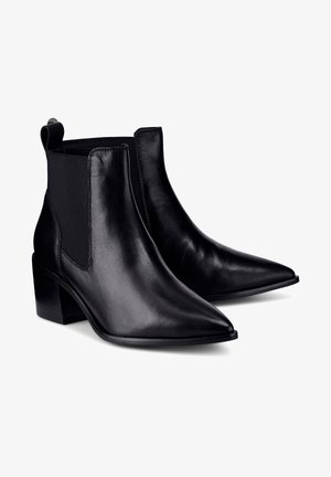 Bottines en cuir noir à bouts pointus, panneaux latéraux élastiques et talons blocs sur fond blanc.