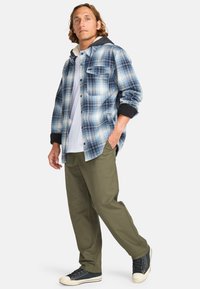 Plaid shirt in blue and white with black sleeves, layered over a white shirt; paired with olive green pants and black sneakers.