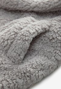 Gros plan d'un tissu sherpa doux, duveteux et gris clair montrant sa texture épaisse, bouclée et ses plis.