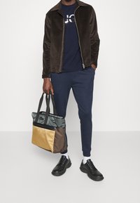 Brown cord jacket, navy t-shirt, navy sweatpants, black shoes, and a multicolored tote bag with gray, brown, and gold sections.